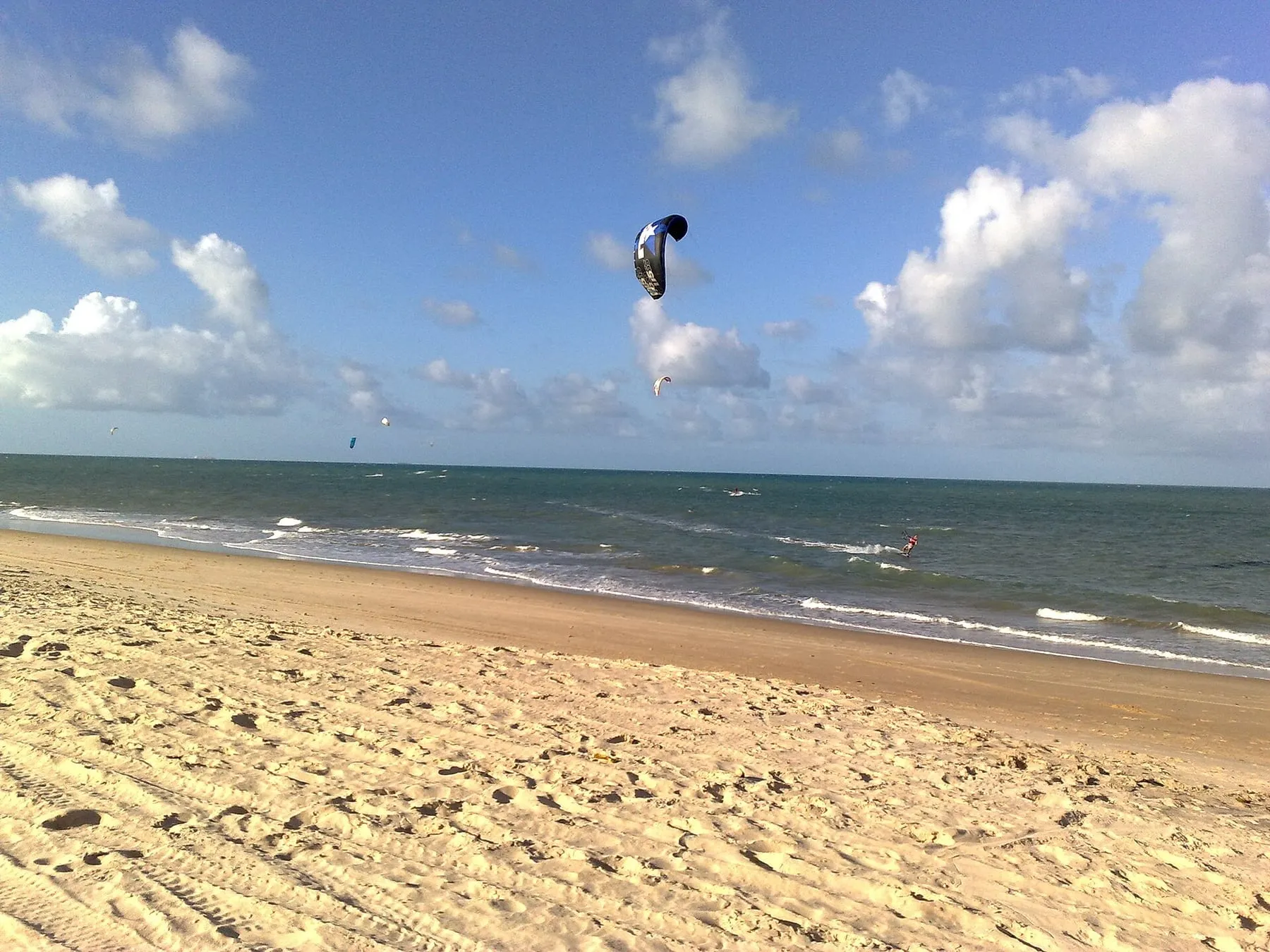 Kitesurfista velejando no mar aberto do Ceará com pipas ao fundo
