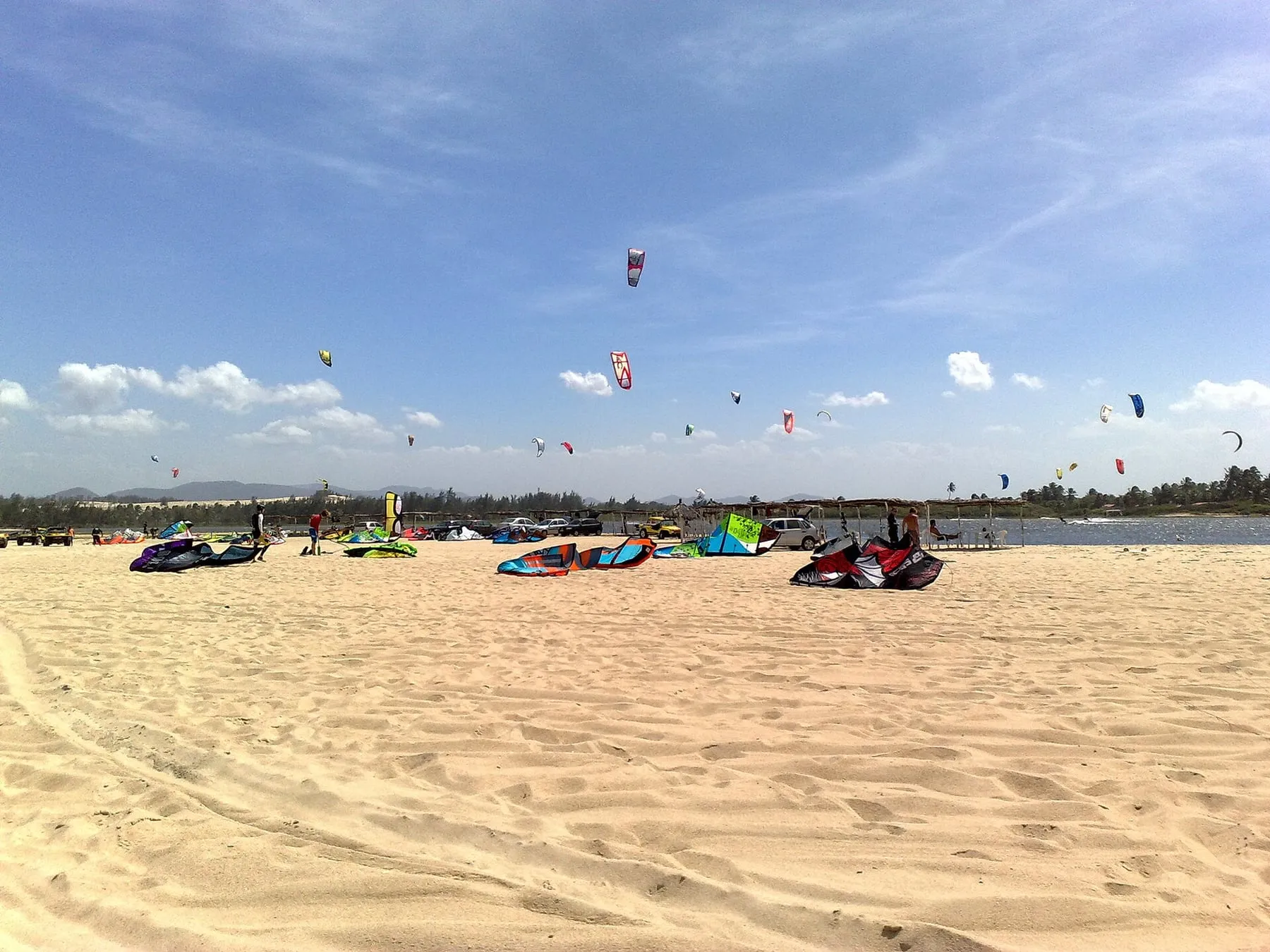 Dezenas de pipas de kitesurf no céu sobre uma praia de areia clara no Ceará